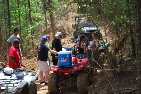 2008 Jeep Wrangler - A group of people stand around several ATVs on a dirt path in a wooded area. One red ATV in the foreground has a blue cooler strapped to it…