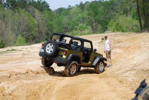 2008 Jeep Wrangler - A green Jeep Wrangler is shown on a dirt trail with a man standing next to it. The Jeep is angled on the trail with its doors open.