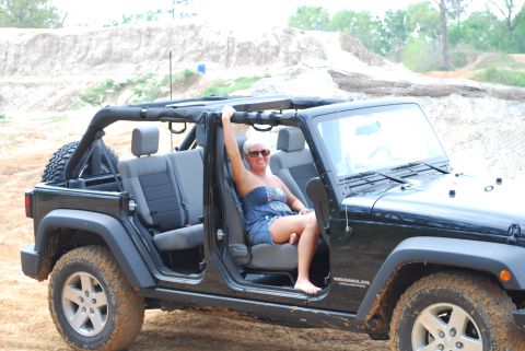 2008 Jeep Wrangler - A black four-door Jeep Wrangler Unlimited JK with doors removed and top folded back sits in a sandy quarry pit, viewed from the side with a…