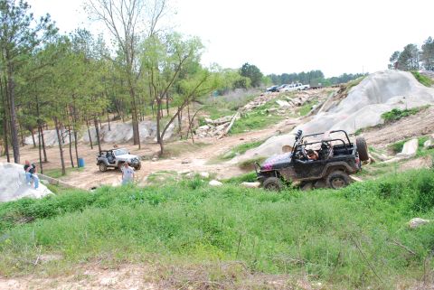 2008 Jeep Wrangler - A black Jeep Wrangler is navigating a rocky, off-road course with a silver Jeep Wrangler parked nearby in a wooded area.