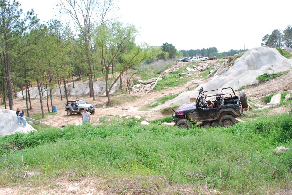 Black Jeep Wrangler off-roading on a rocky trail with a silver Jeep in the background.