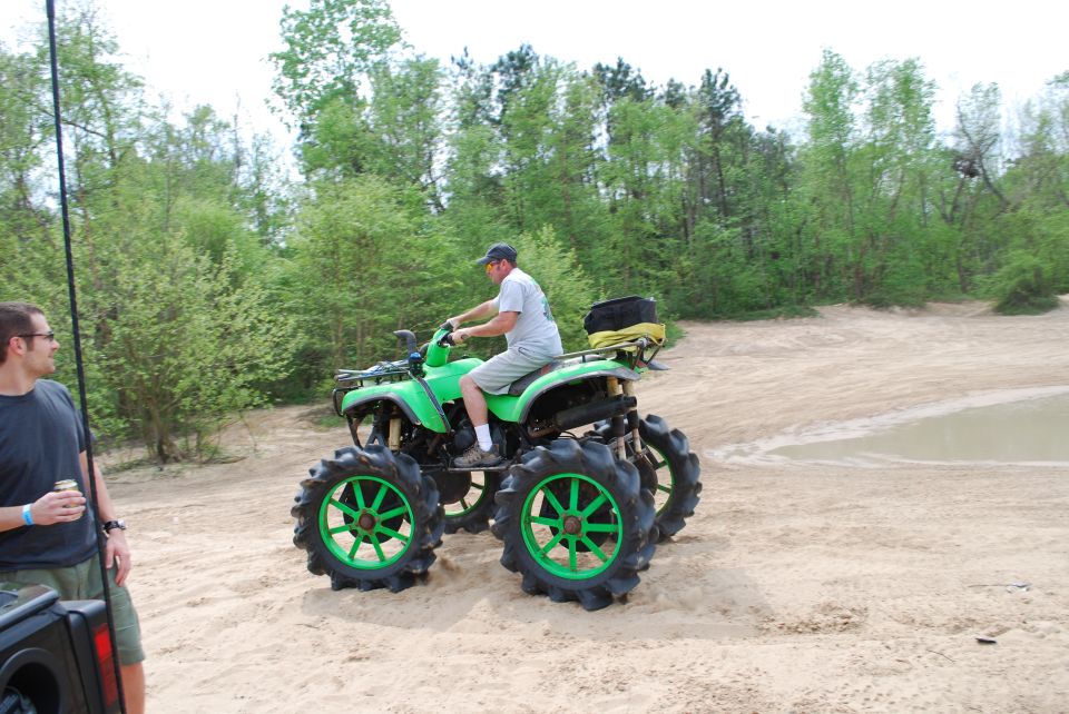 Green ATV with large tires on a sandy trail, man riding, man standing nearby.
