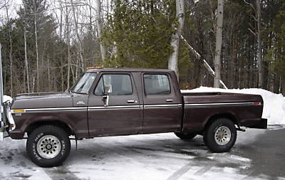 1979 Ford F-250 - A brown 1970s four-door pickup truck is parked on a snow-covered road with trees in the background.