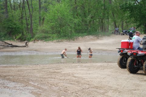 2008 Jeep Wrangler - Several ATVs are parked on a sandy track near a muddy waterhole where three people are wading. One ATV in the foreground has a red cooler m…