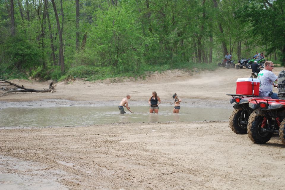 ATVs parked near a waterhole with people wading.
