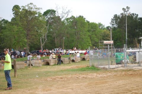 2008 Jeep Wrangler - A crowd of people are gathered around a muddy track with a wooded background. Several vehicles are parked in the background.