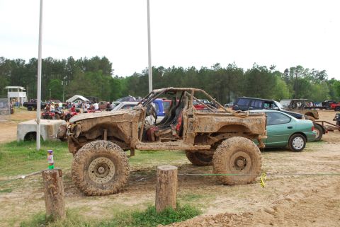 2008 Jeep Wrangler - A heavily mud-covered off-road vehicle with a roll cage and exposed interior sits in a dirt lot. Other vehicles and trees are visible in th…