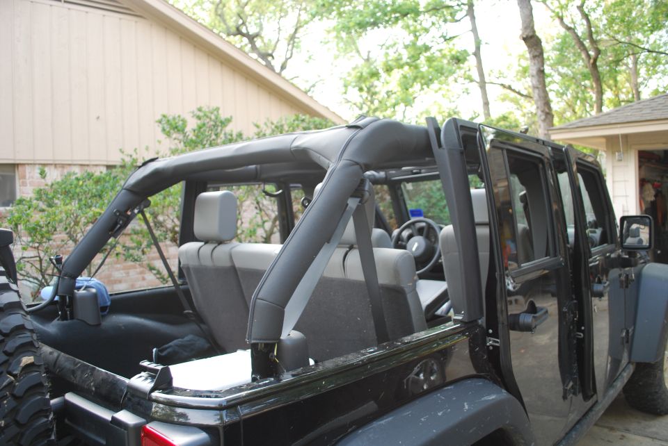Black Jeep Wrangler interior with roll cage and rear seats, doors removed.