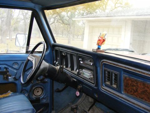 1979 Ford Bronco - The interior of a blue vintage Ford truck or SUV is shown, focusing on the dashboard and driver's side door. A dashboard ornament of a cowb…