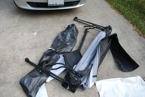 2008 Jeep Wrangler - A disassembled canopy structure with black and gray fabric components and black metal poles are laid out on a concrete surface next to a si…
