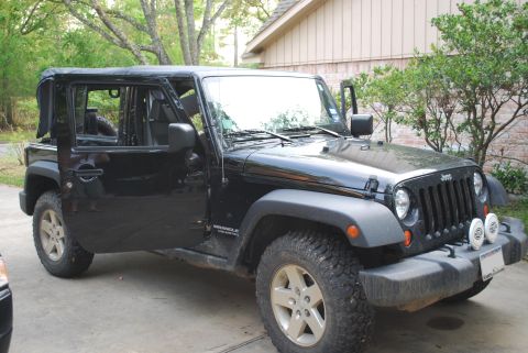 2008 Jeep Wrangler - A black four-door Jeep Wrangler Unlimited JK parked on a driveway with its doors removed and soft top folded back, shown from the front thr…