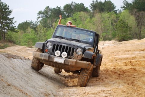 2008 Jeep Wrangler - A black Jeep Wrangler is driving off-road on a dirt and sand trail, with two people inside. The driver is visible, and a passenger is leani…