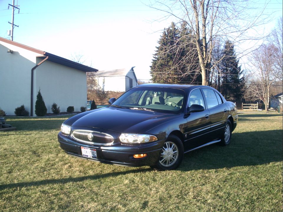 Dark blue Buick LeSabre sedan on a lawn, front three-quarter view with headlights on