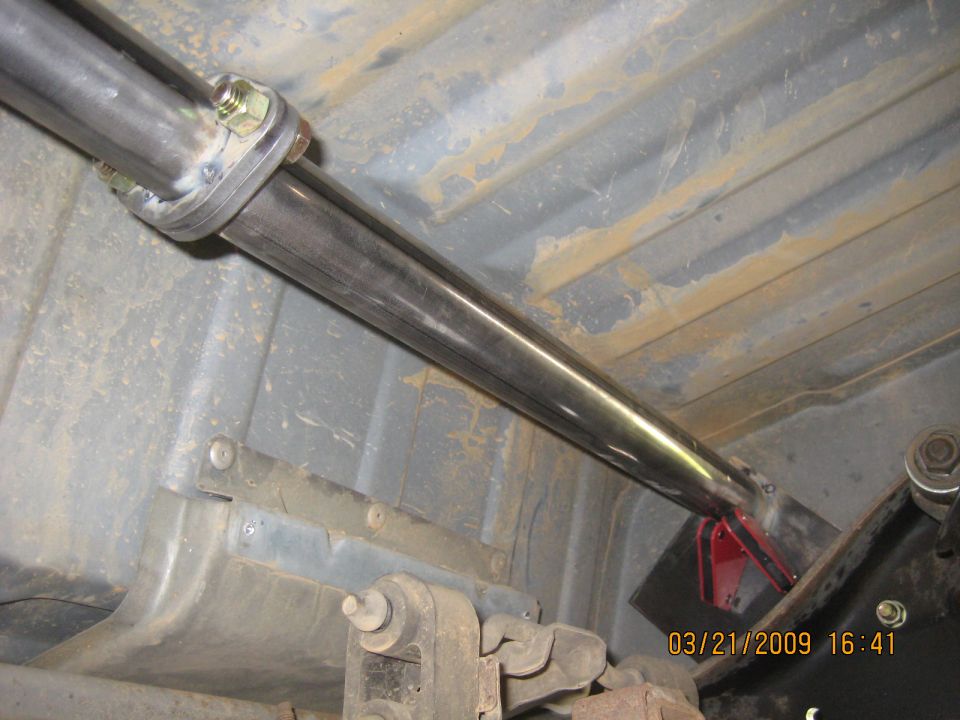 Underside of a vehicle showing a custom exhaust pipe with a flange connection and red support bracket.