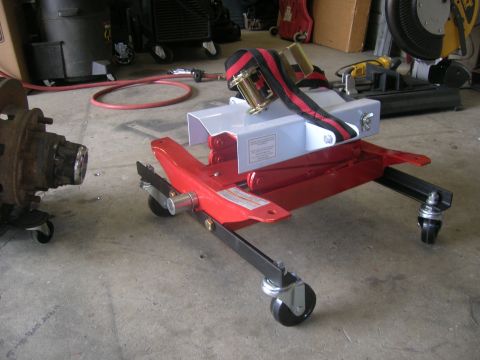 1996 Ford Bronco - A red transmission jack and a differential are on a concrete floor in a workshop.