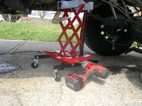 1996 Ford Bronco - A red scissor jack and impact wrench are positioned under the underbody of a vehicle.