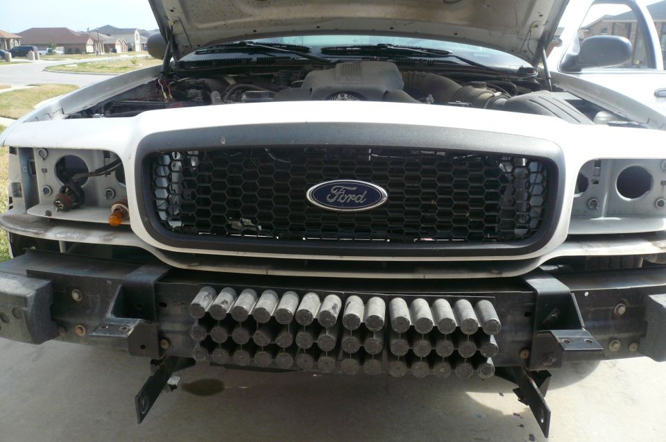 White Ford sedan front end with hood up, headlights and bumper cover removed, exposing crash absorber tubes