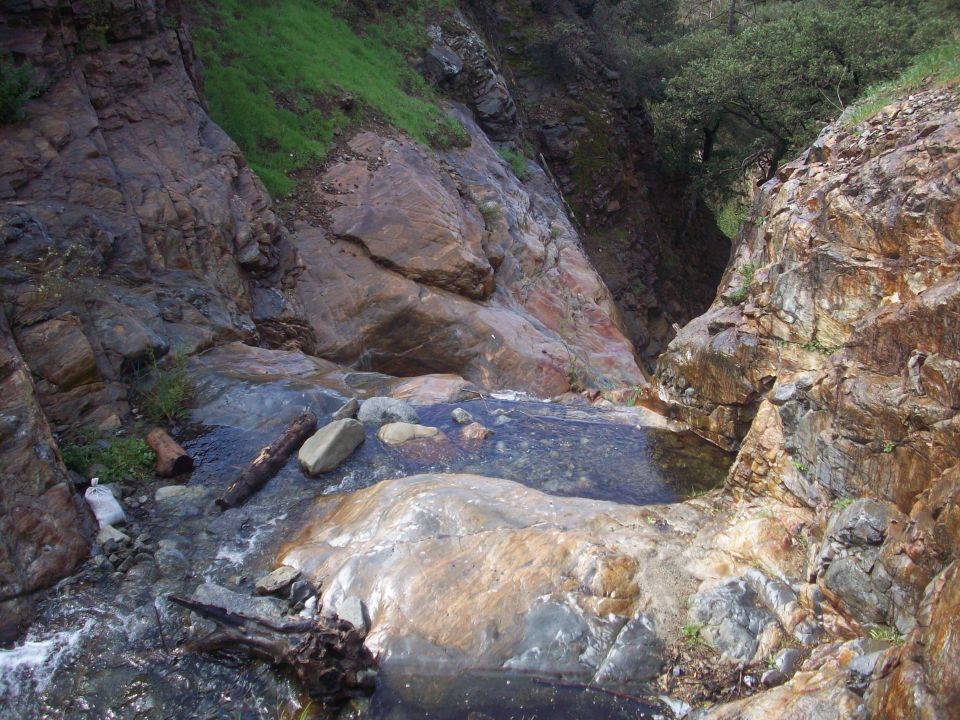 Rocky stream bed with water flowing over rocks and vegetation on the slopes