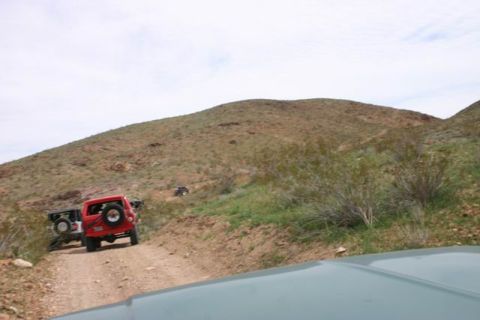 1991 Ford Bronco - Two SUVs navigate a dusty, hilly terrain on a bright, overcast day.