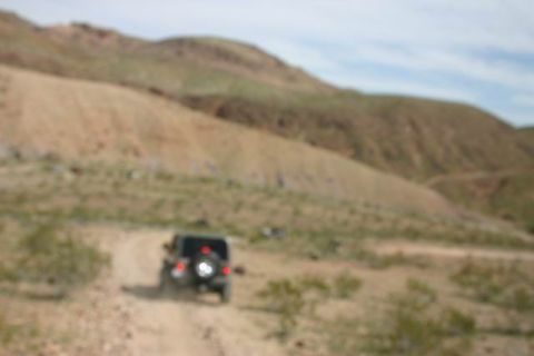 1991 Ford Bronco - A Jeep Wrangler navigates a dusty trail through a barren, hilly terrain under a cloudy sky.