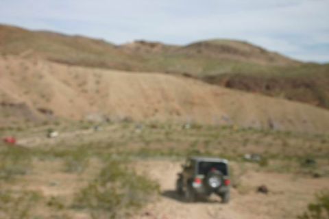 1991 Ford Bronco - Several vehicles are visible in the distance on a dusty, arid terrain under a hazy sky.