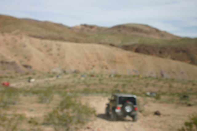 Dark gray Jeep Wrangler driving on a dirt road in a desert landscape