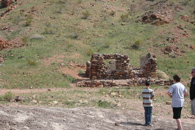 Stone ruins stand in a dry, grassy landscape with three people observing