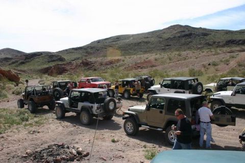 1991 Ford Bronco - A convoy of off-road vehicles is gathered on a dusty trail under a partly cloudy sky.
