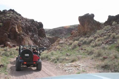 1991 Ford Bronco - Two Jeeps navigate a rocky off-road trail through a canyon under a bright sky.