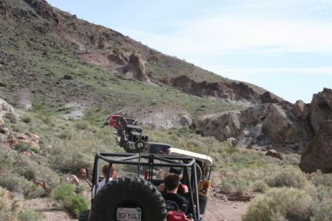1991 Ford Bronco - Multiple off-road vehicles navigate a steep, rocky trail in a mountainous desert landscape.