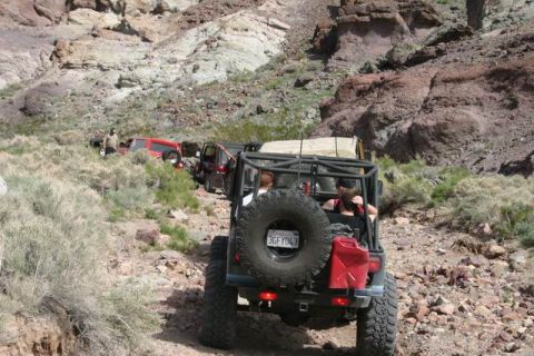 1991 Ford Bronco - A line of off-road vehicles navigates a canyon path, kicking up dust on the trail.