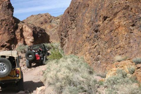 1991 Ford Bronco - Two off-road vehicles navigate a narrow, rocky canyon trail under a clear blue sky. The Supermotors.net logo is visible in the lower right…