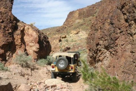 1991 Ford Bronco - A Jeep navigates a canyon trail under a clear blue sky.