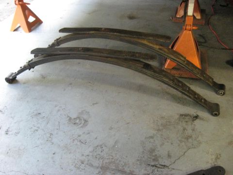 1991 Ford Bronco - Leaf springs are shown resting on a concrete floor, with orange jack stands visible in the background.
