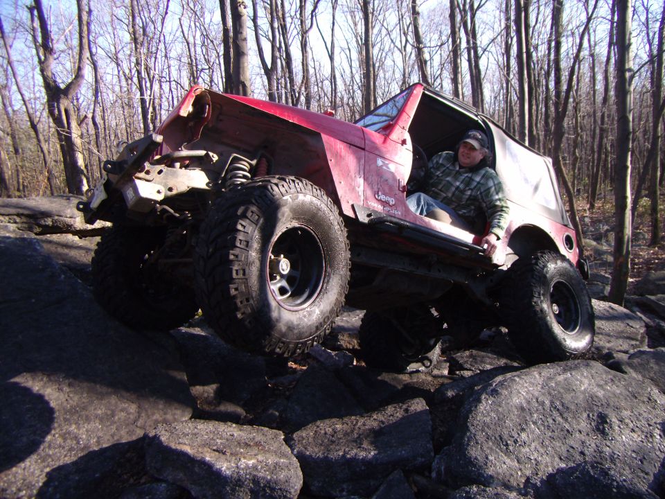 Red 2003 Jeep Wrangler with a damaged front end, on rocks, driver seated
