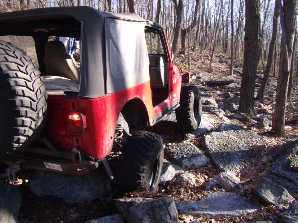 Red Jeep Wrangler on rocky trail, soft top up