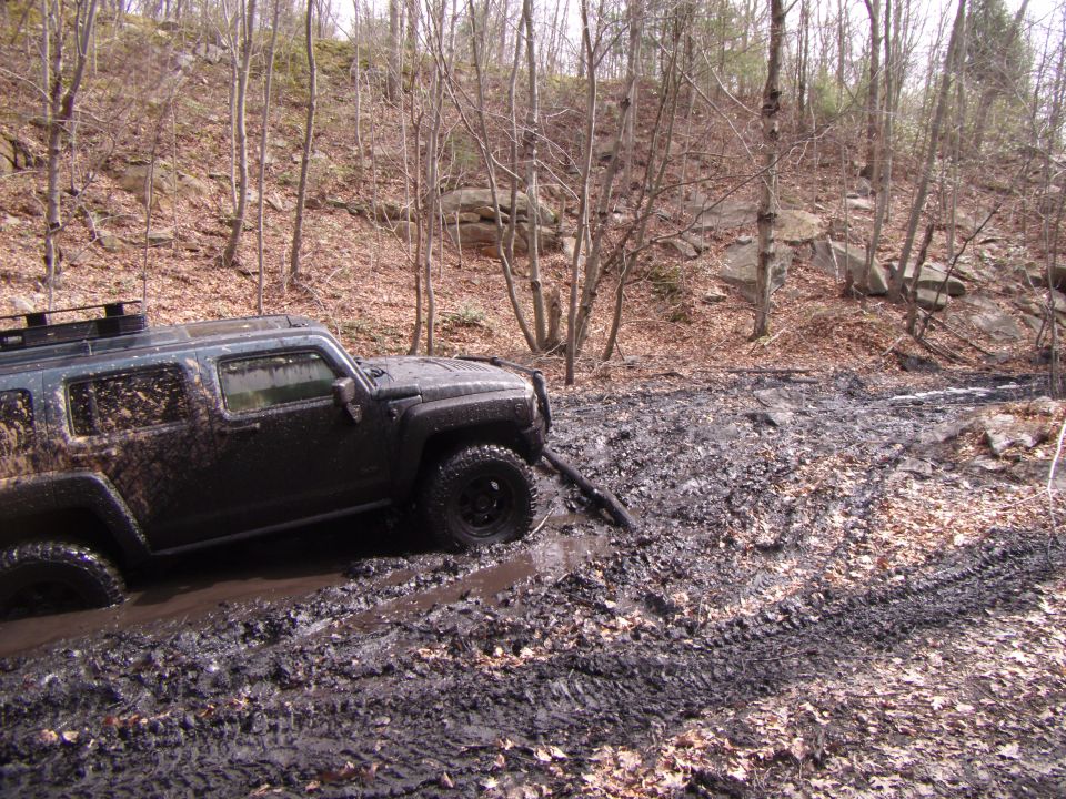 Mud-covered dark gray Hummer H3 stuck in mud on a wooded trail
