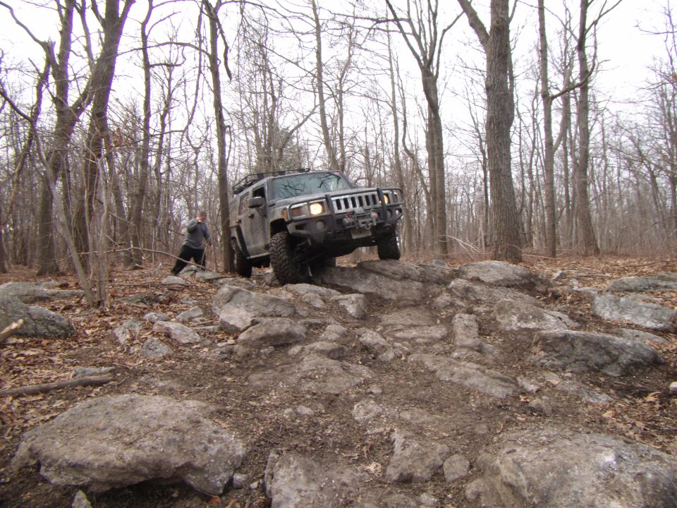 Gray Hummer H3 off-roading on a rocky trail, front-right tire elevated