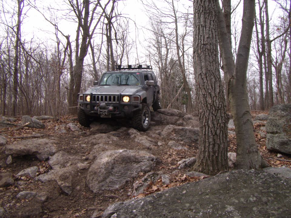 Gray SUV with roof rack navigating rocks off-road. Supermotors.net logo visible