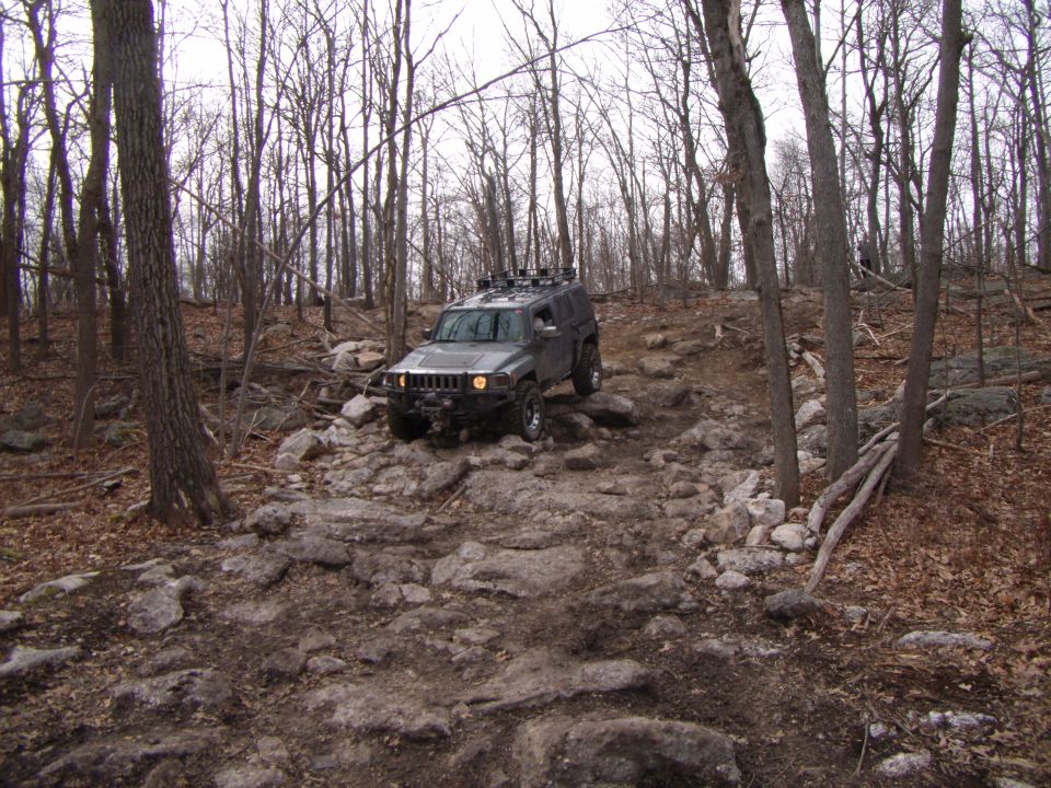 Hummer H3 navigating a rocky off-road trail in a wooded area