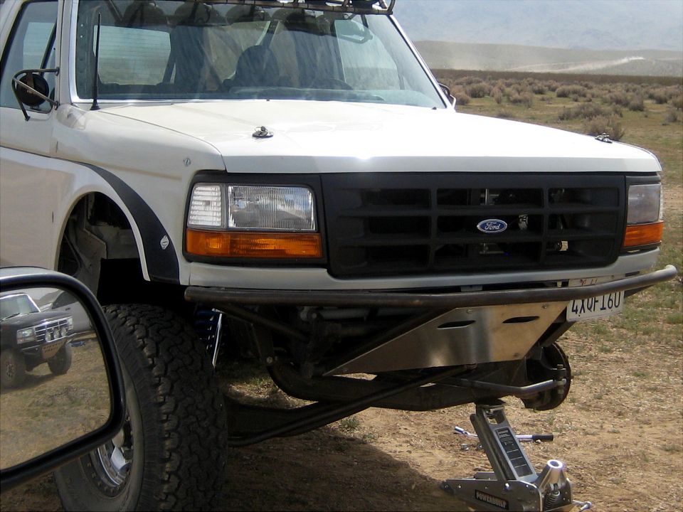 White Ford Bronco front with tubular bumper, blue shocks, on jack in desert