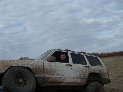 1987 Ford Bronco - A man smiles from inside a heavily mud-covered white SUV during an off-road excursion.