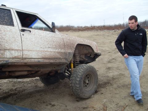 1987 Ford Bronco - Mud-covered Jeep Cherokee XJ with a man standing next to it on a dirt lot.