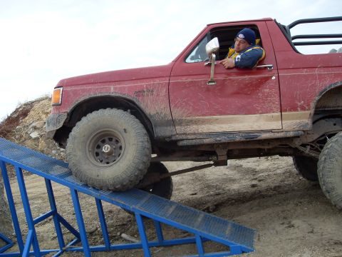 1987 Ford Bronco - A driver maneuvers a red Ford Bronco up a blue ramp during an off-road event.