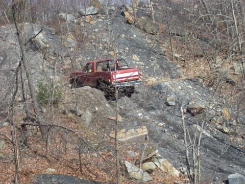 1987 Ford Bronco - A red pickup truck navigates a steep, rocky terrain.