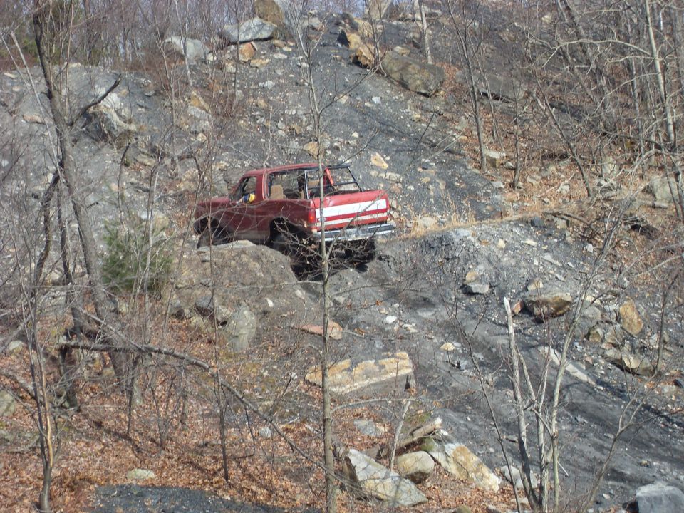 Red pickup truck with white stripe on the side, driving on a rocky incline