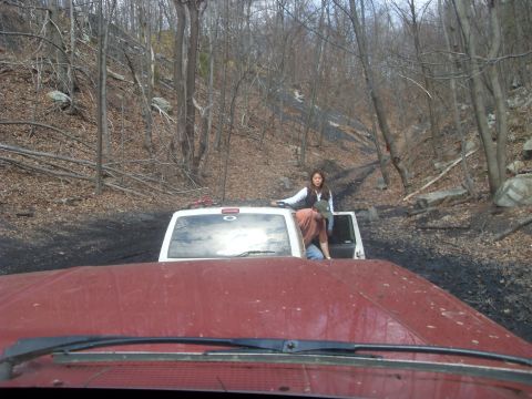 1987 Ford Bronco - Two people are in and on a white SUV navigating a muddy, wooded trail.
