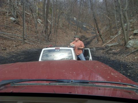 1987 Ford Bronco - Two vehicles navigate a muddy, wooded trail during an off-road excursion.