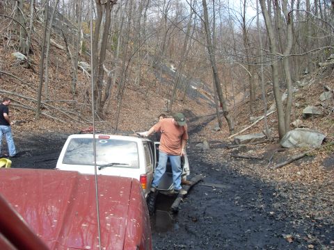 1987 Ford Bronco - Several off-road vehicles navigate a challenging muddy trail through a dense forest.