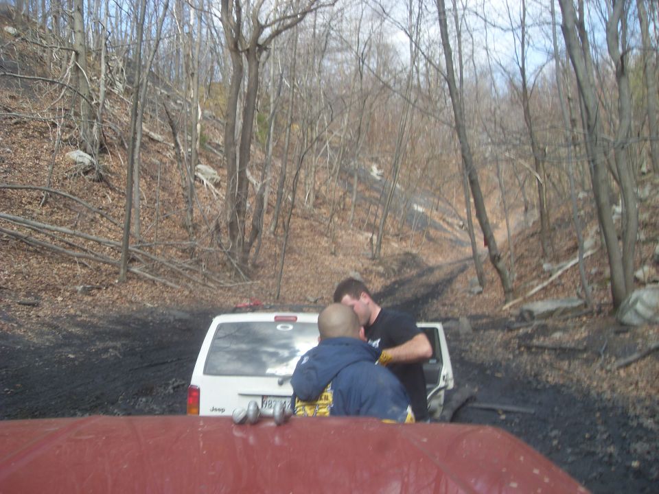White Jeep Cherokee rear view with two men standing behind it on a dirt road